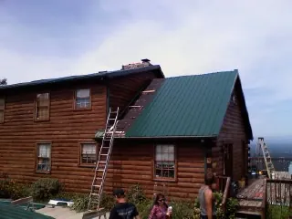 Green metal roof going on a two story log home with ladders set in Mashantucket